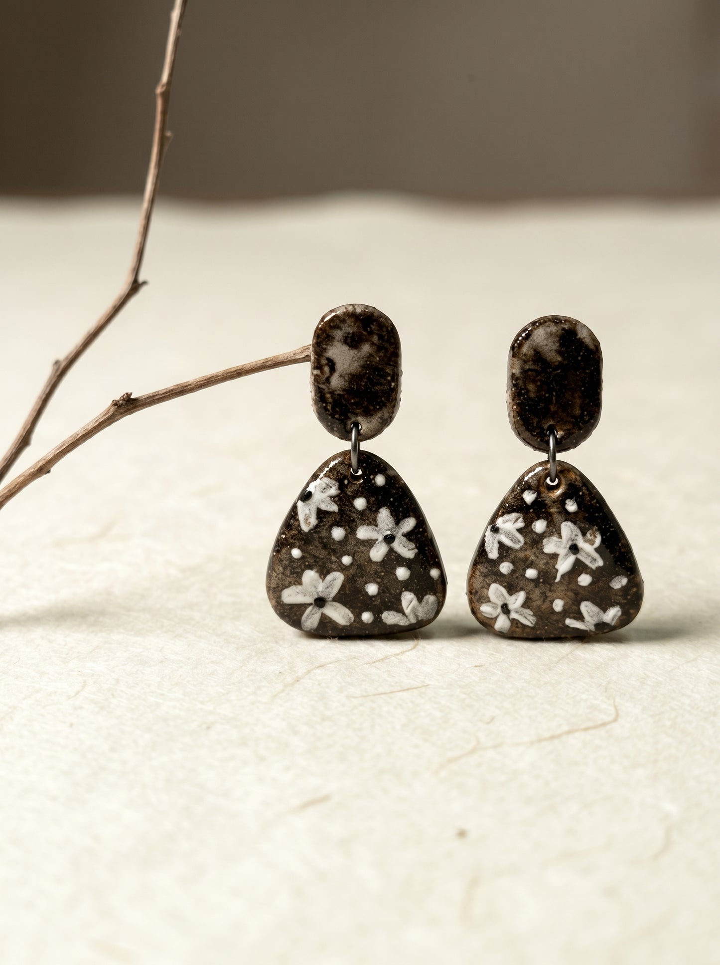 Close-up of a HECROWN ceramic earring on rough stone, highlighting the hammered black top and beige speckled polka dot texture. Authentic handcrafted artisan jewelry details.