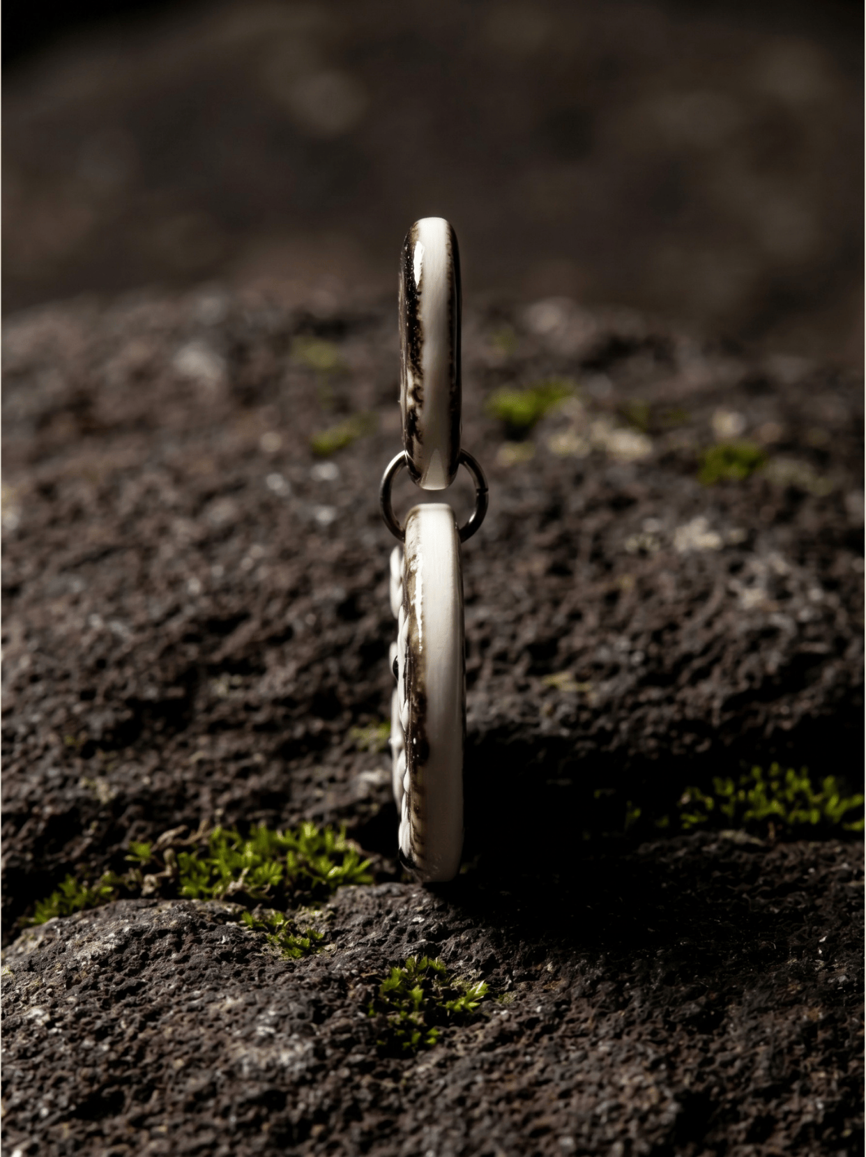 Side view of a HECROWN hand-painted ceramic earring resting on dark volcanic rock with moss. Showcasing the precise artisan thickness and honest craftsmanship of Jingdezhen ceramic art.