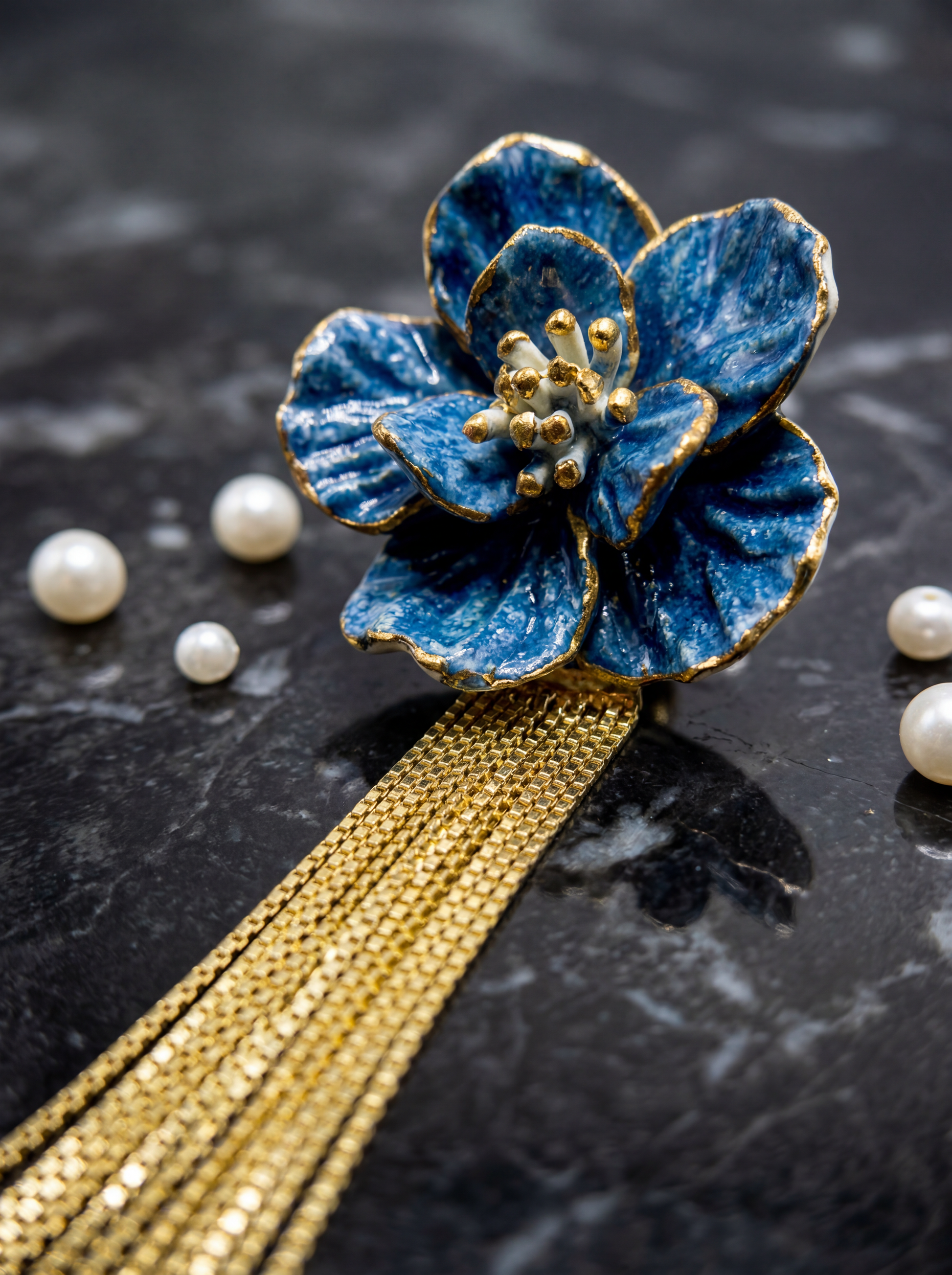A single Blue Bloom ceramic earring with gold tassels displayed on black marble with scattered pearls. An elegant handmade jewelry piece perfect for anniversary gifts.