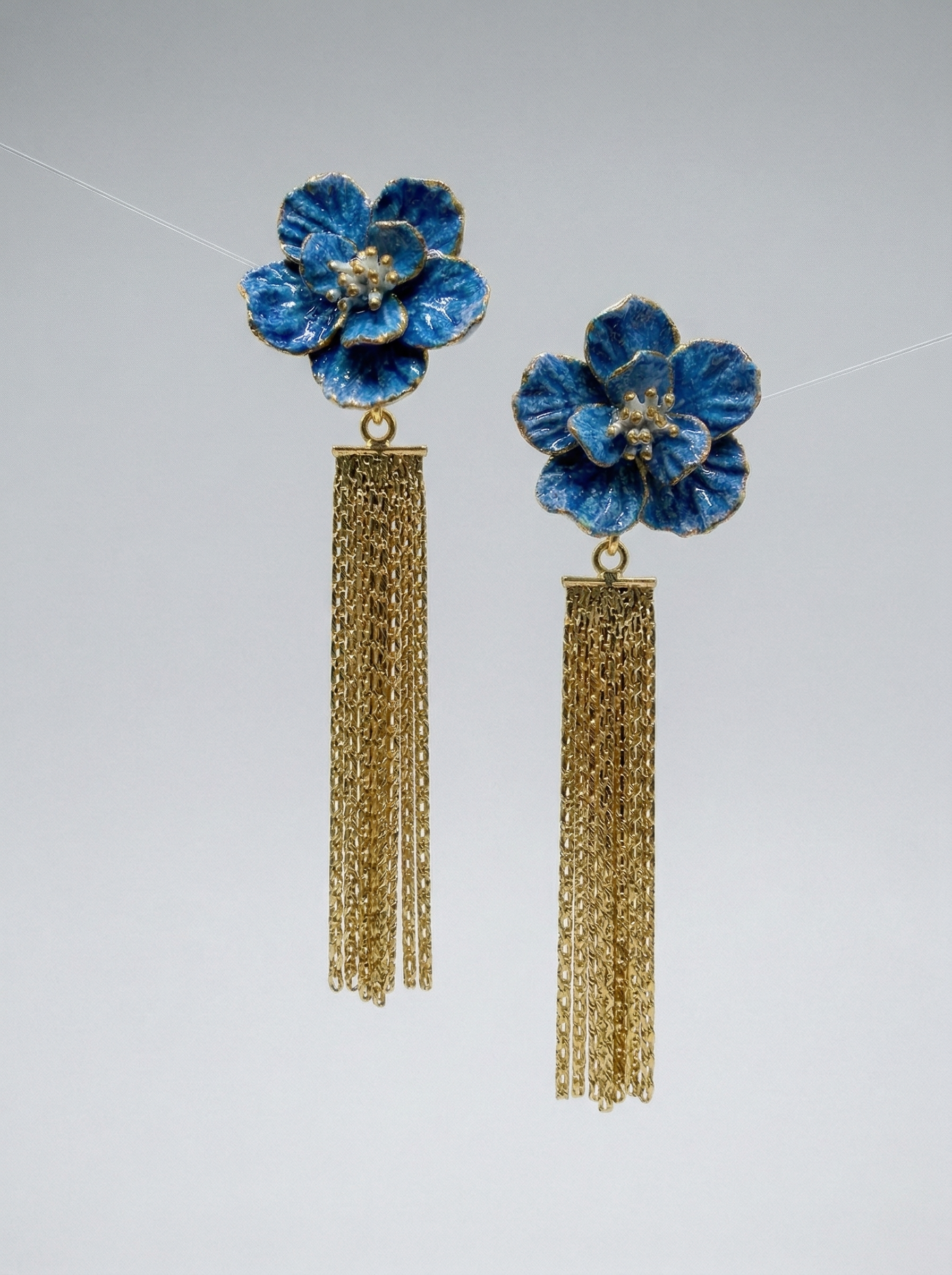 Two Blue Bloom ceramic earrings with long gold tassels suspended against a clean background. A unique Valentine's Day gift option for lovers of high-end handmade jewelry and Jingdezhen ceramics.