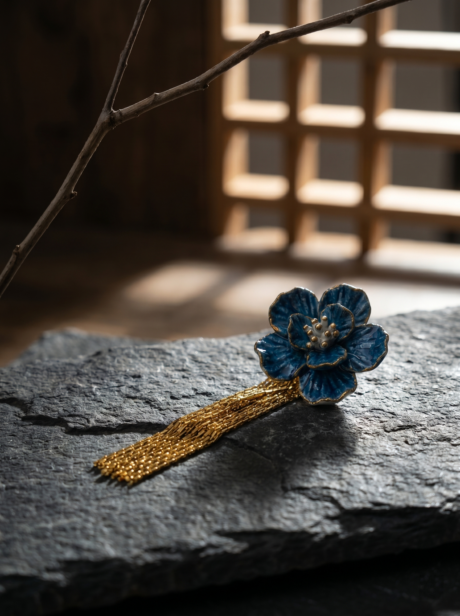 A single HECROWN blue flower earring with gold tassels on a rough stone surface. The perfect Valentine's Day gift showcasing the texture of Jingdezhen porcelain.