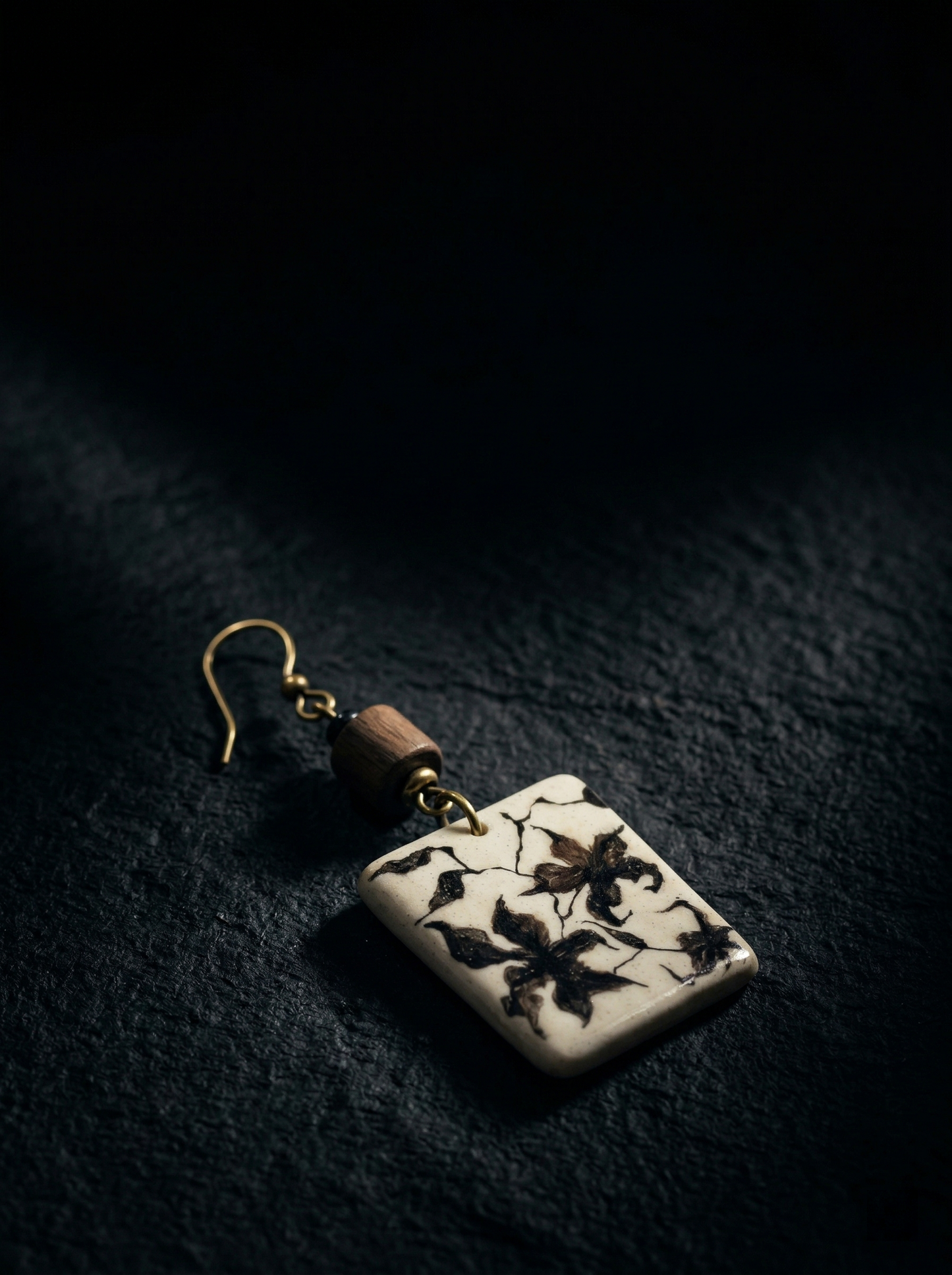 A single HECROWN vintage ceramic earring with hand-painted black floral patterns and a wooden bead, resting on dark slate. Sincere Jingdezhen handmade jewelry, perfect for a unique anniversary gift.