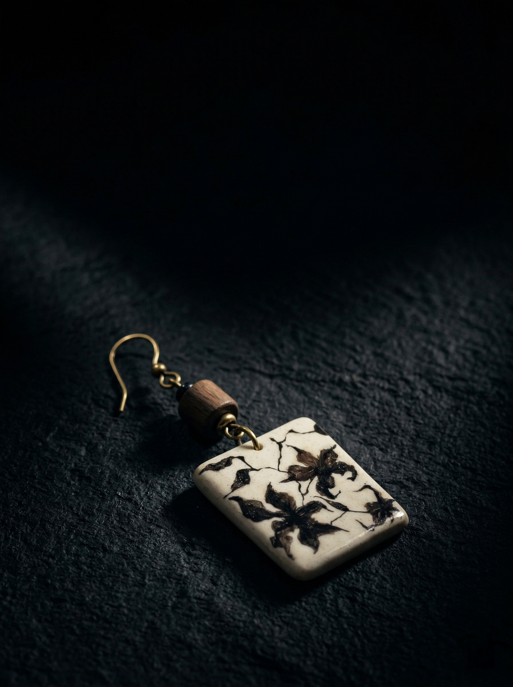 A single HECROWN vintage ceramic earring with hand-painted black floral patterns and a wooden bead, resting on dark slate. Sincere Jingdezhen handmade jewelry, perfect for a unique anniversary gift.