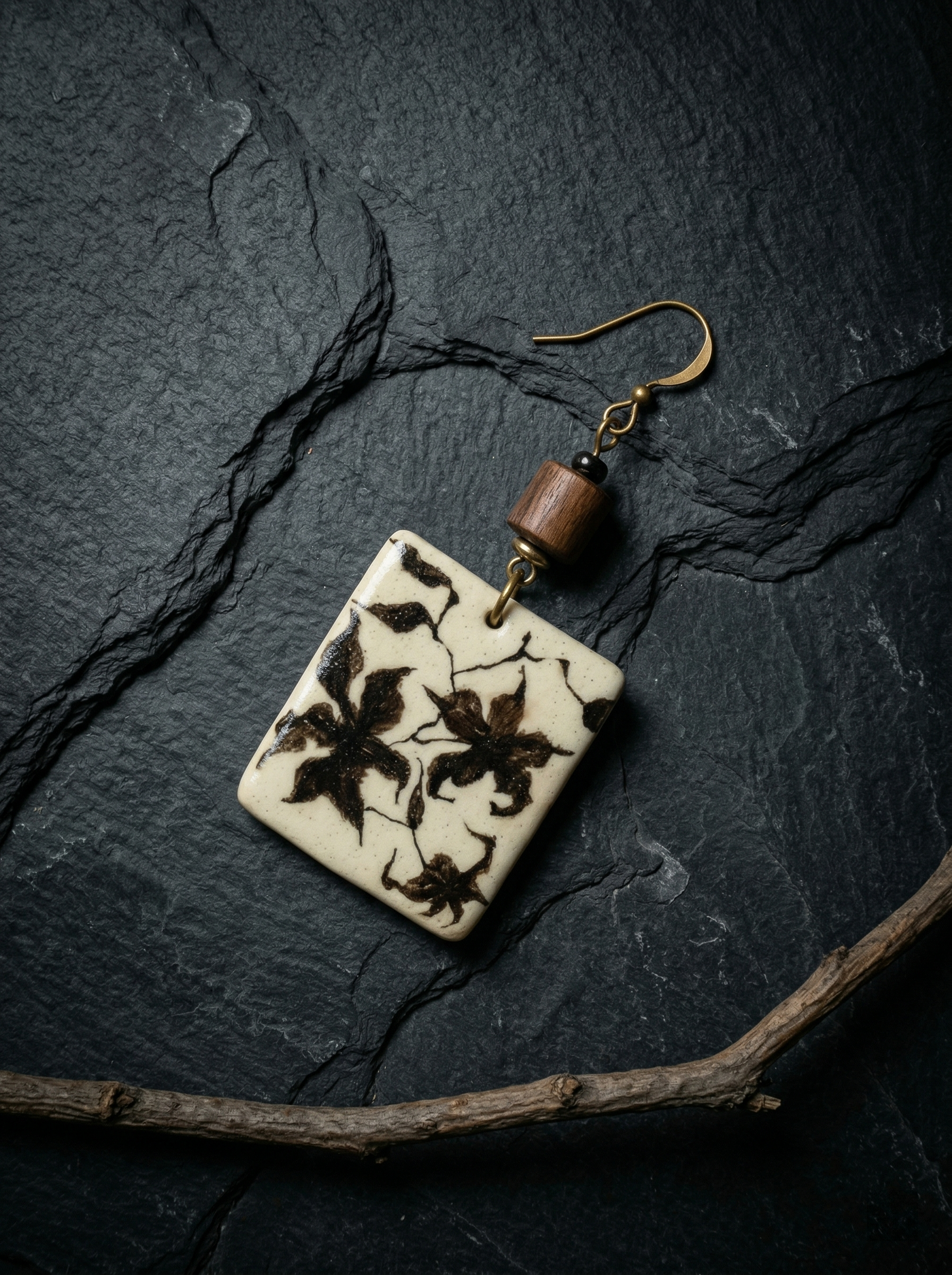 Single HECROWN hand-painted ceramic earring with a black floral motif and wooden bead on dark slate. Authentic Jingdezhen handmade jewelry showcasing a moody, vintage artisan aesthetic.