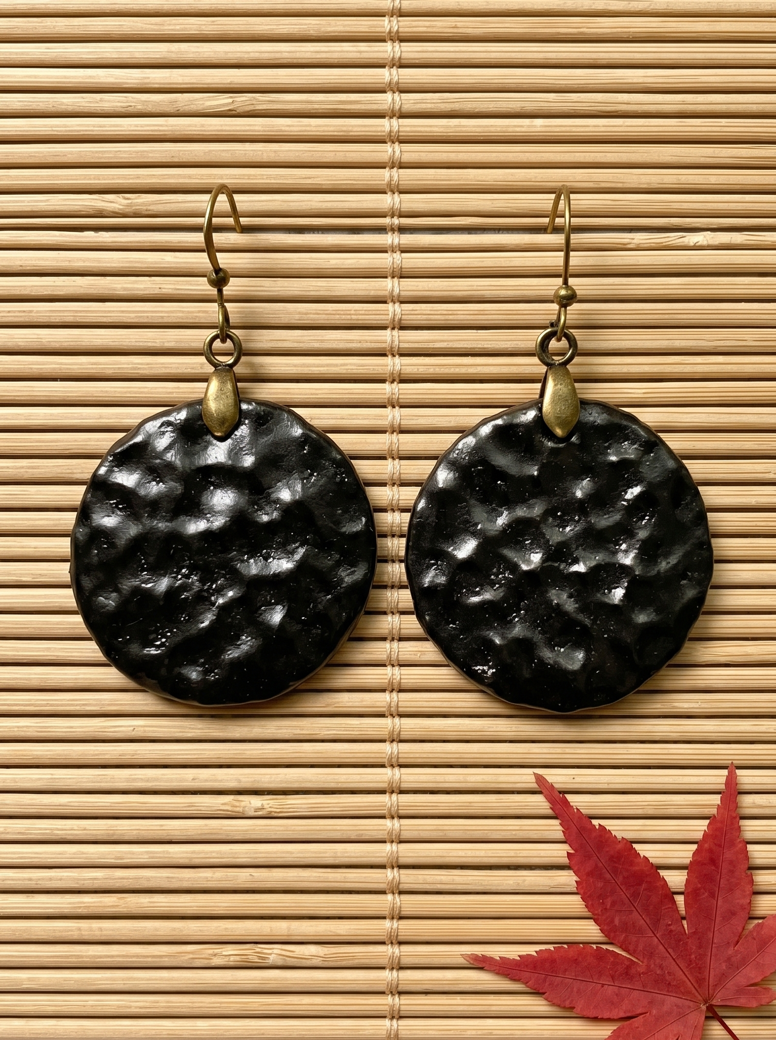 A pair of HECROWN round black hammered ceramic earrings resting on a dark wood tray. Authentic Jingdezhen handmade jewelry and a unique anniversary gift.