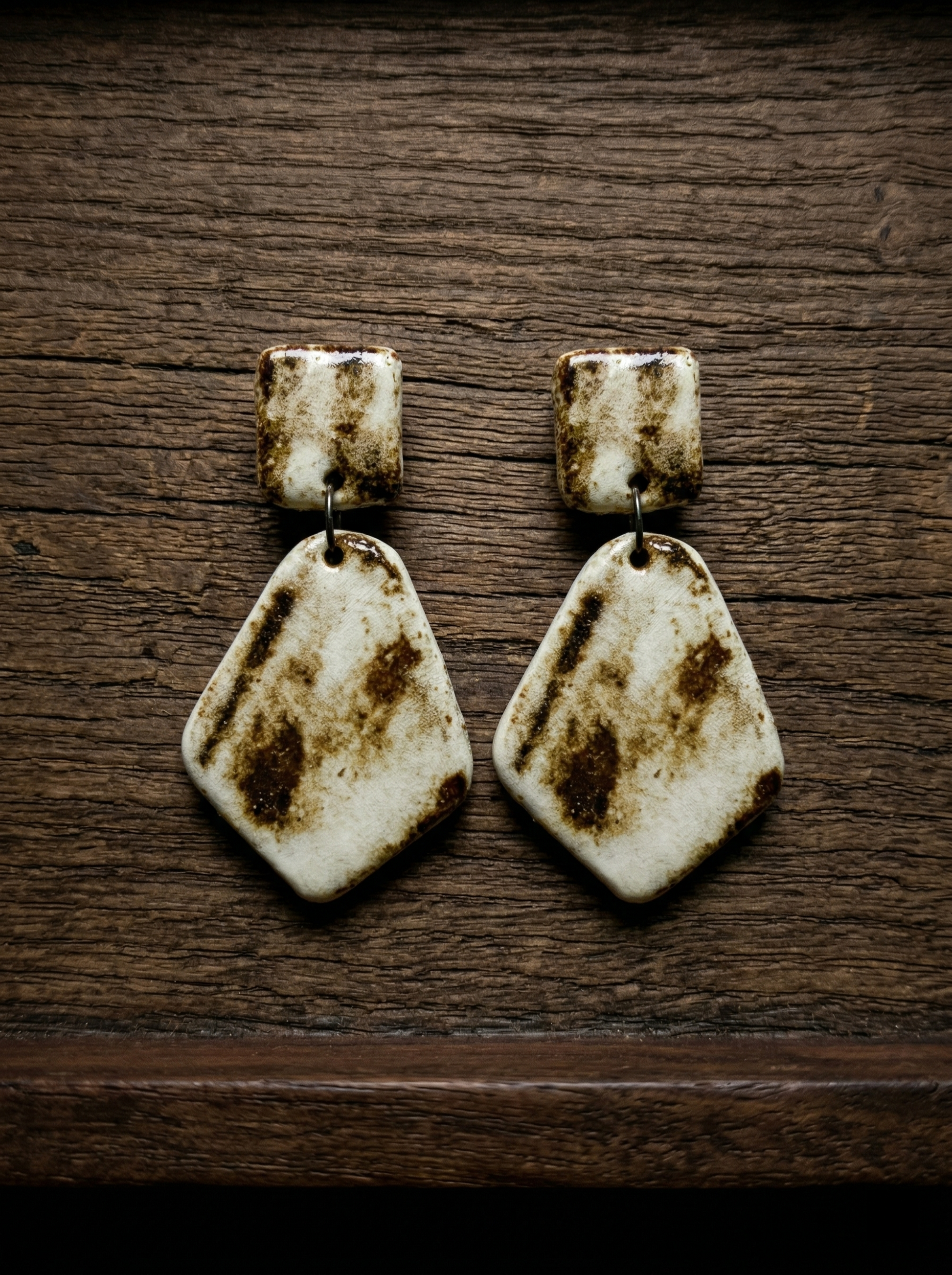 A pair of HECROWN rustic geometric ceramic earrings on dark wood. Featuring a natural burnt glaze effect, showcasing the wabi-sabi aesthetic of Jingdezhen handmade jewelry. A unique artisan gift.