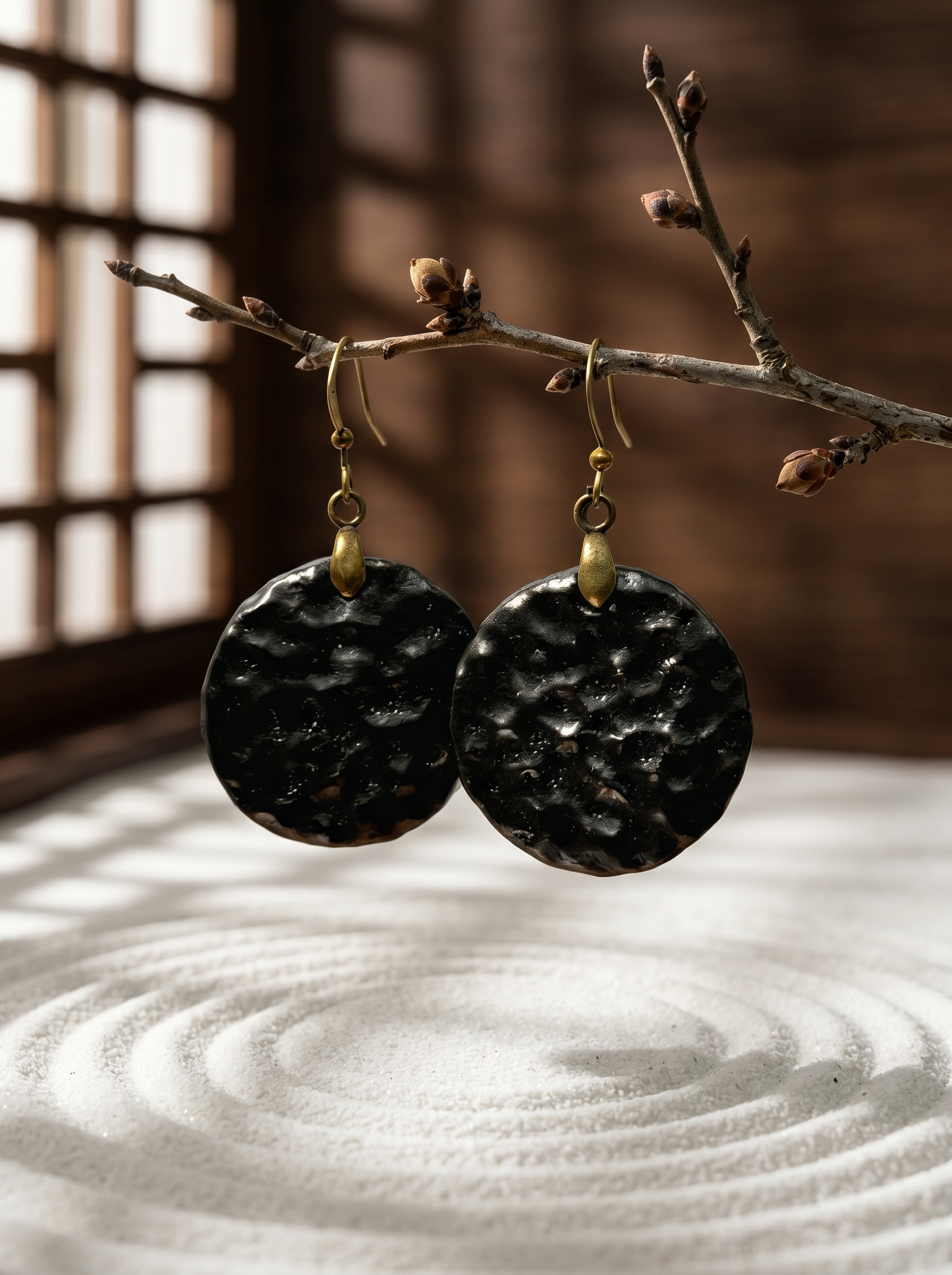 HECROWN black hammered ceramic earrings suspended from a branch over a zen sand garden. Showcasing the tranquil aesthetic of Jingdezhen handcrafted jewelry.