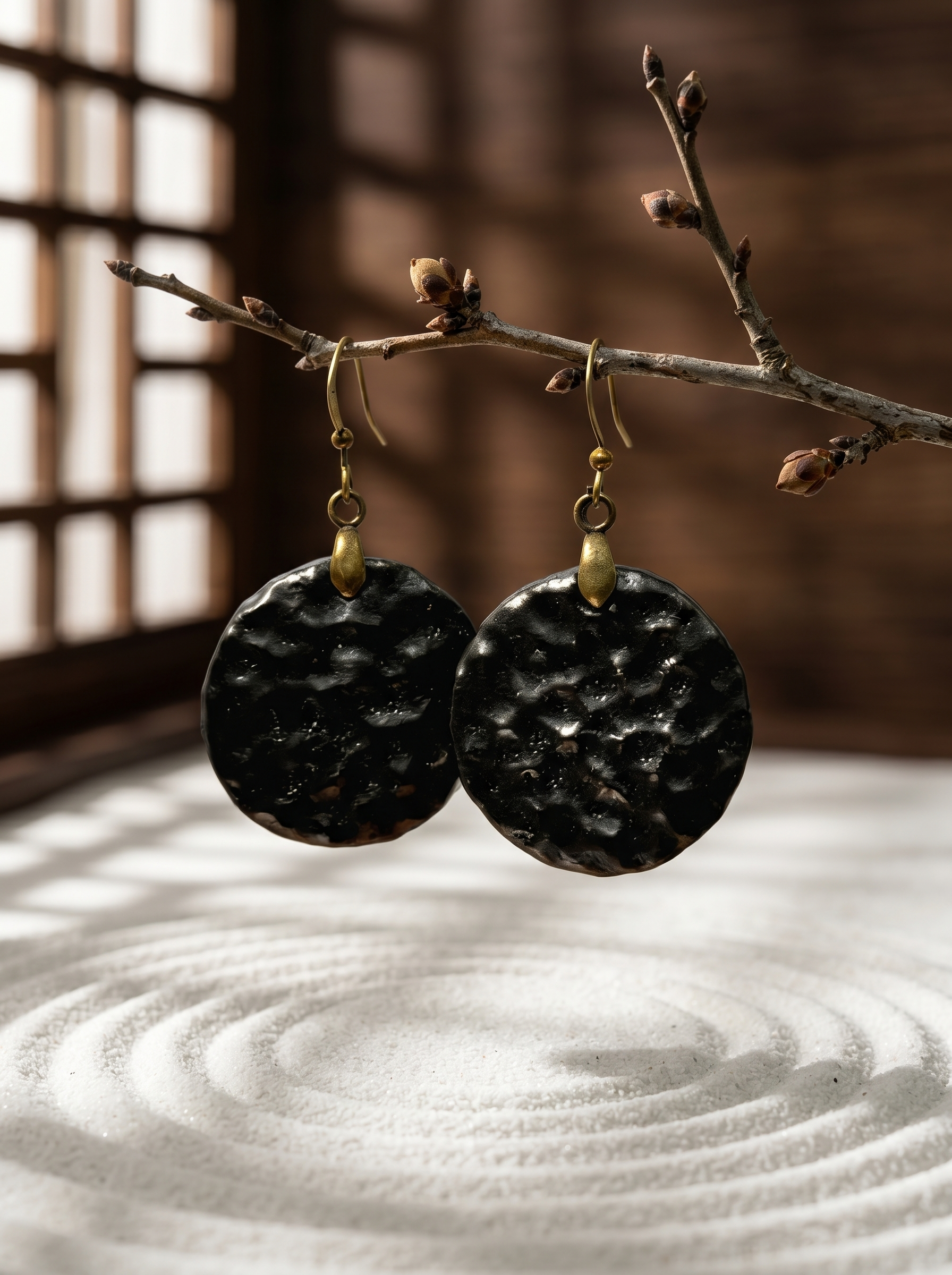 HECROWN black hammered ceramic earrings suspended from a branch over a zen sand garden. Showcasing the tranquil aesthetic of Jingdezhen handcrafted jewelry.